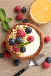 Photo of Tasty yogurt with granola, honey and berries in bowl on wooden table, flat lay