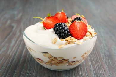 Photo of Tasty yogurt with granola and berries in bowl on wooden table, closeup