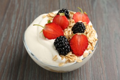 Photo of Tasty yogurt with granola and berries in bowl on wooden table, closeup