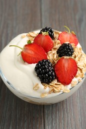 Photo of Tasty yogurt with granola and berries in bowl on wooden table, closeup