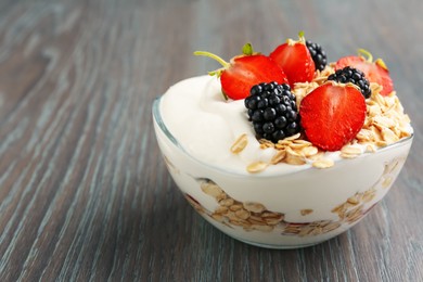 Photo of Tasty yogurt with granola and berries in bowl on wooden table, closeup. Space for text
