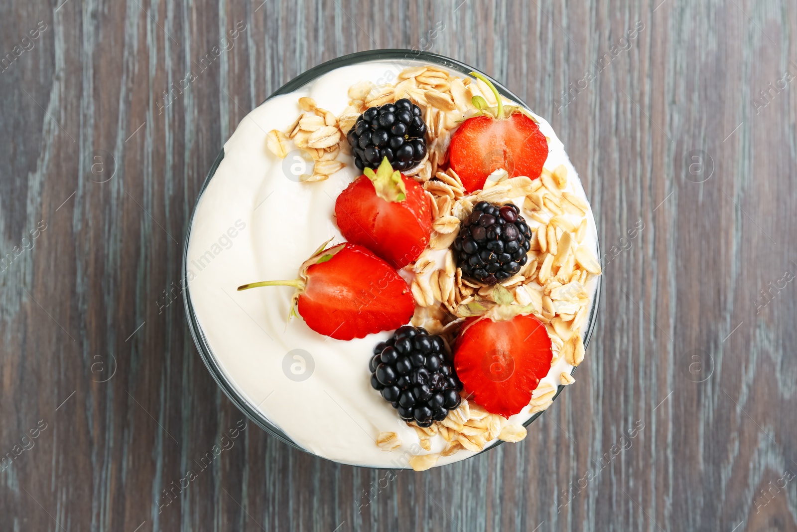 Tasty yogurt with granola and berries in bowl on wooden table, top view Photo of Tasty yogurt with granola and berries in bowl on wooden table, top view