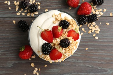 Photo of Tasty yogurt with granola and berries in bowl on wooden table, flat lay