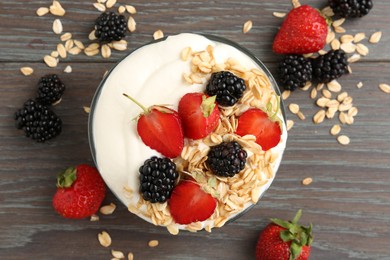 Photo of Tasty yogurt with granola and berries in bowl on wooden table, flat lay