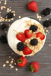 Photo of Tasty yogurt with granola and berries in bowl on wooden table, flat lay