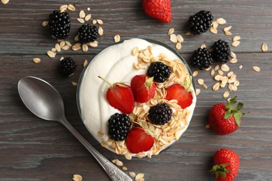 Photo of Tasty yogurt with granola and berries in bowl on wooden table, flat lay