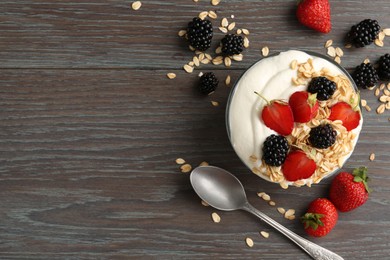 Photo of Tasty yogurt with granola and berries in bowl on wooden table, flat lay. Space for text