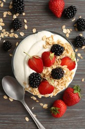 Photo of Tasty yogurt with granola and berries in bowl on wooden table, flat lay