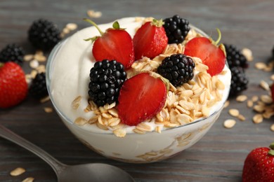 Photo of Tasty yogurt with granola and berries in bowl on wooden table, closeup