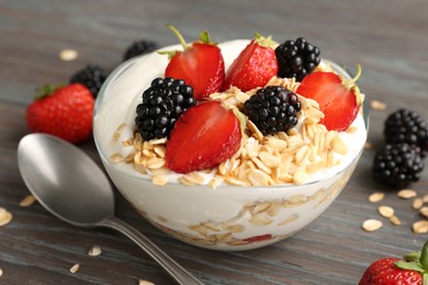 Photo of Tasty yogurt with granola and berries in bowl on wooden table, closeup