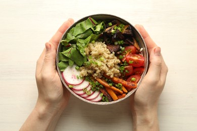 Photo of Healthy vegetarian food. Woman with delicious Buddha bowl at light wooden table, top view