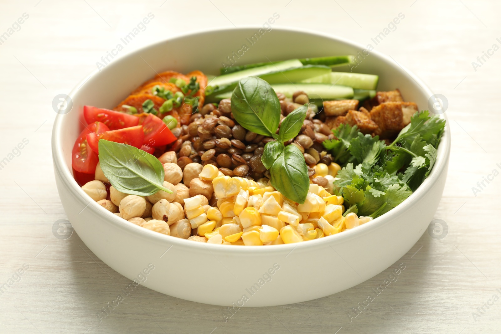 Photo of Healthy vegetarian food. Delicious Buddha bowl with lentils, tofu, chickpeas and vegetables on light wooden table, closeup