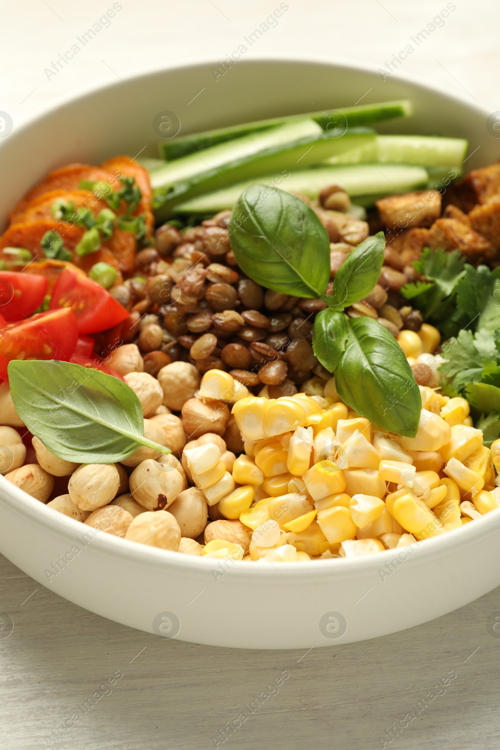 Photo of Healthy vegetarian food. Delicious Buddha bowl with lentils, tofu, chickpeas and vegetables on light wooden table, closeup