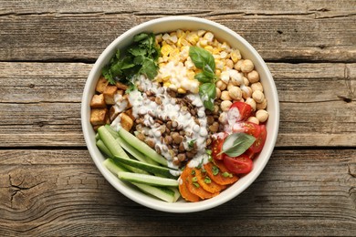Photo of Healthy vegetarian food. Delicious Buddha bowl with lentils, tofu, chickpeas, vegetables and sauce on wooden table, top view