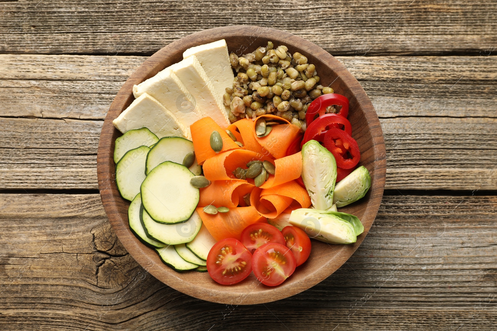 Photo of Healthy vegetarian food. Delicious Buddha bowl with lentils, tofu and vegetables on wooden table, top view