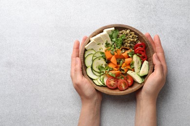 Photo of Healthy vegetarian food. Woman with delicious Buddha bowl at light grey table, top view. Space for text