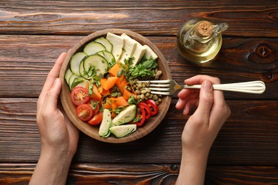 Photo of Healthy vegetarian food. Woman eating delicious Buddha bowl at wooden table, top view