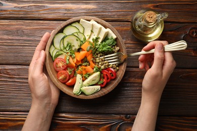 Photo of Healthy vegetarian food. Woman eating delicious Buddha bowl at wooden table, top view