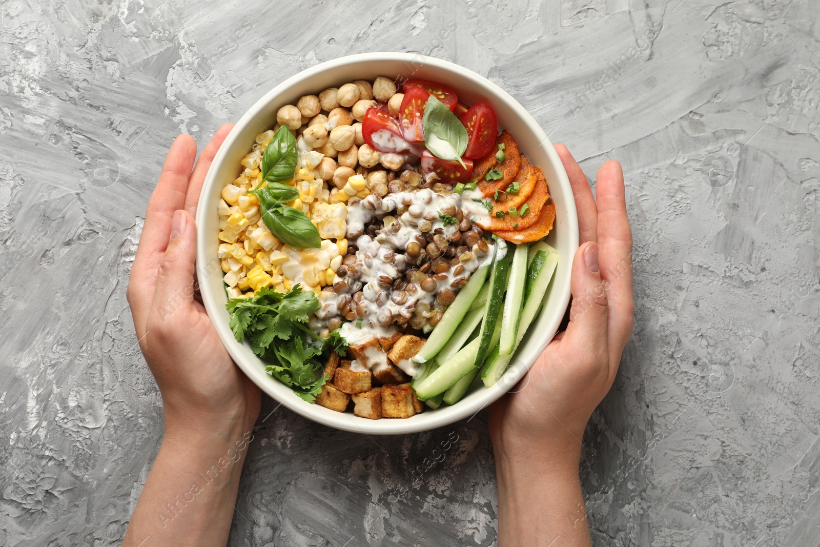 Healthy vegetarian food. Woman with delicious Buddha bowl at grey table, top view Photo of Healthy vegetarian food. Woman with delicious Buddha bowl at grey table, top view