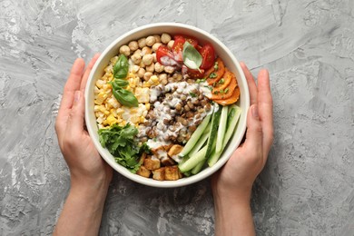 Photo of Healthy vegetarian food. Woman with delicious Buddha bowl at grey table, top view