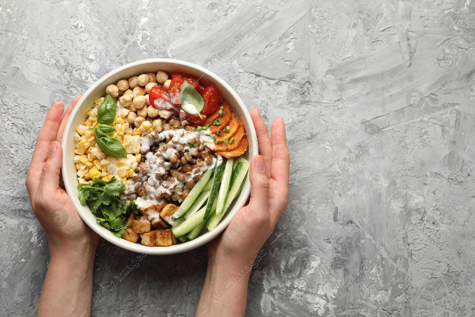 Healthy vegetarian food. Woman with delicious Buddha bowl at grey table, top view. Space for text Photo of Healthy vegetarian food. Woman with delicious Buddha bowl at grey table, top view. Space for text
