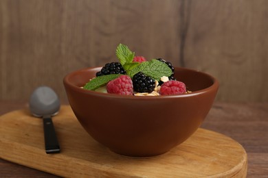 Photo of Tasty yogurt with granola and berries in bowl on wooden table, closeup