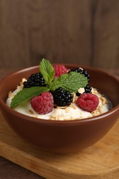 Photo of Tasty yogurt with granola and berries in bowl on wooden table, closeup