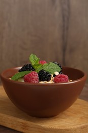 Photo of Tasty yogurt with granola and berries in bowl on wooden table, closeup