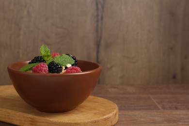 Photo of Tasty yogurt with granola and berries in bowl on wooden table, closeup. Space for text