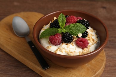 Photo of Tasty yogurt with granola and berries in bowl on wooden table, closeup