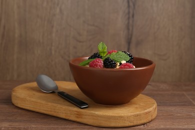 Photo of Tasty yogurt with granola and berries in bowl on wooden table, closeup