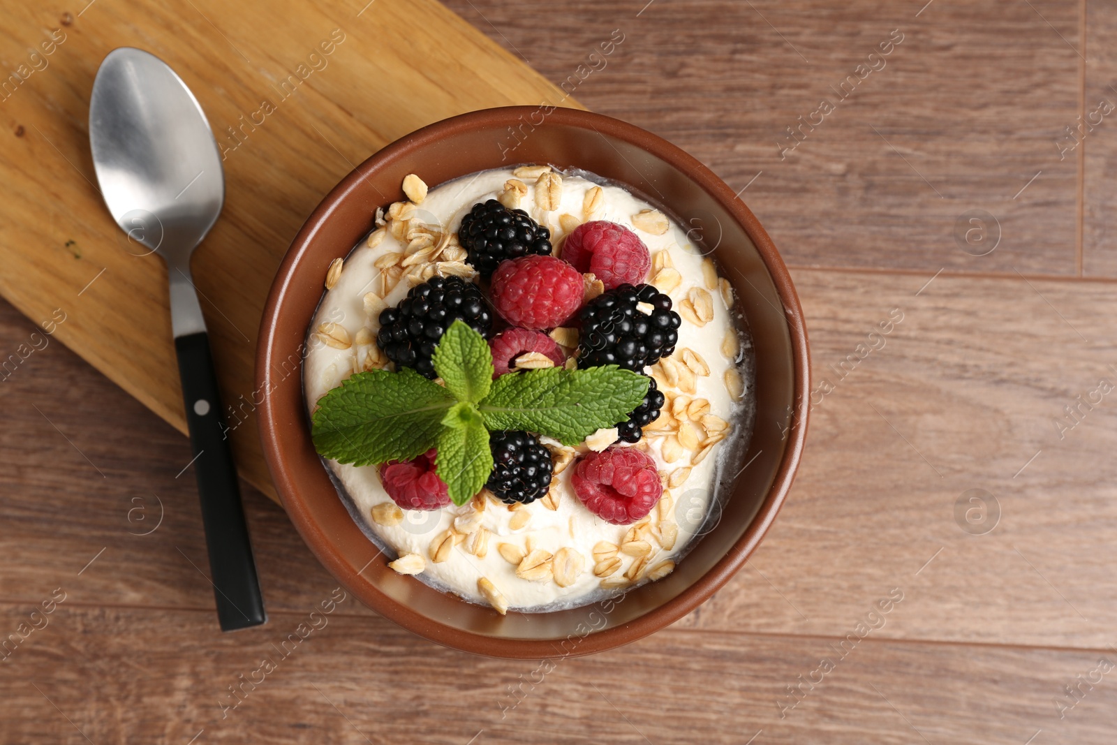 Photo of Tasty yogurt with granola and berries in bowl on wooden table, top view