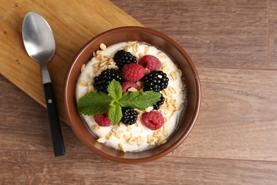 Photo of Tasty yogurt with granola and berries in bowl on wooden table, top view