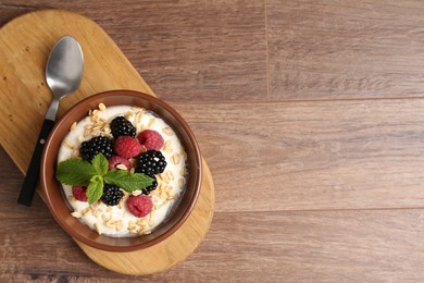 Photo of Tasty yogurt with granola and berries in bowl on wooden table, top view. Space for text