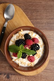 Photo of Tasty yogurt with granola and berries in bowl on wooden table, top view