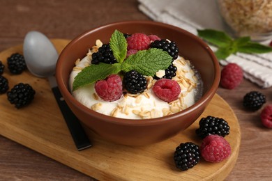 Photo of Tasty yogurt with granola and berries in bowl on wooden table, closeup