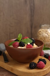 Photo of Tasty yogurt with granola and berries in bowl on wooden table, closeup. Space for text