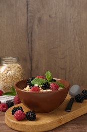 Photo of Tasty yogurt with granola and berries in bowl on wooden table, closeup. Space for text
