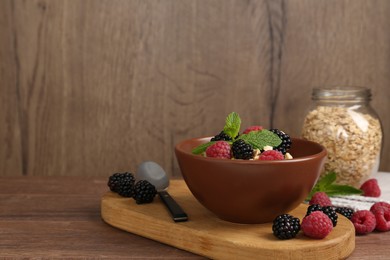 Photo of Tasty yogurt with granola and berries in bowl on wooden table, closeup. Space for text