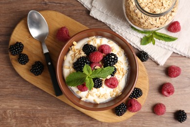 Photo of Tasty yogurt with granola and berries in bowl on wooden table, flat lay