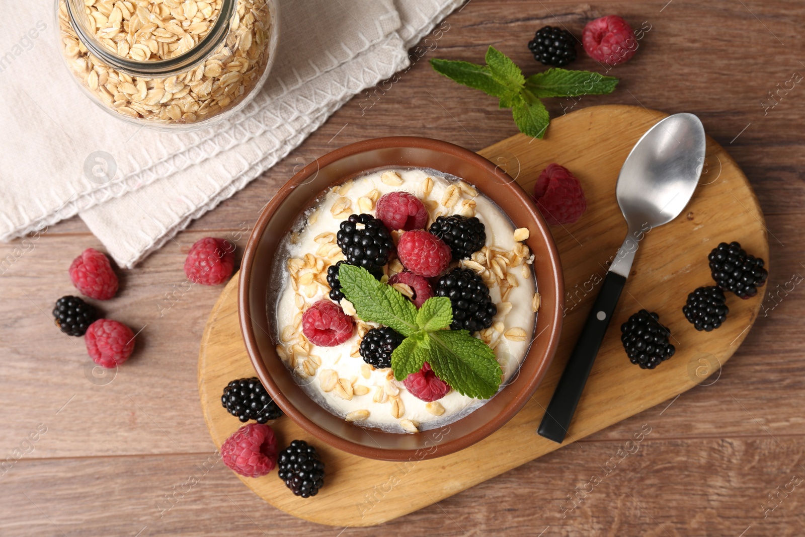 Tasty yogurt with granola and berries in bowl on wooden table, flat lay Photo of Tasty yogurt with granola and berries in bowl on wooden table, flat lay