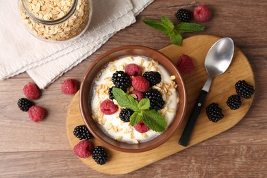Photo of Tasty yogurt with granola and berries in bowl on wooden table, flat lay