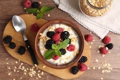Photo of Tasty yogurt with granola and berries in bowl on wooden table, flat lay