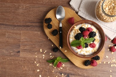 Photo of Tasty yogurt with granola and berries in bowl on wooden table, flat lay. Space for text
