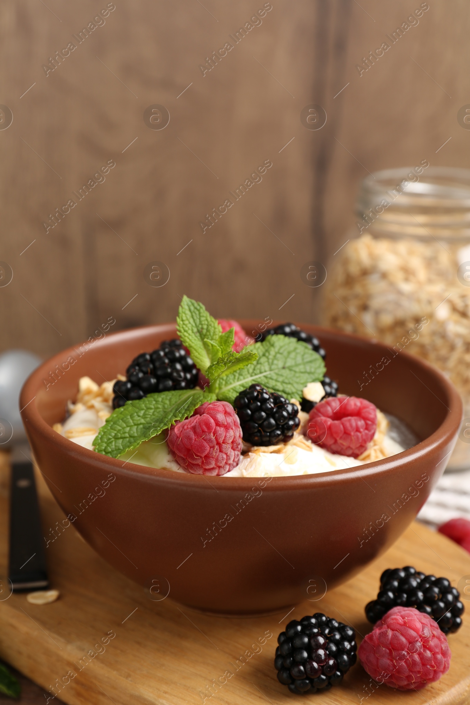 Photo of Tasty yogurt with granola and berries in bowl on wooden table, closeup