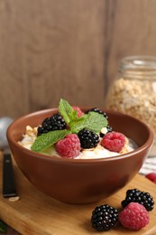 Photo of Tasty yogurt with granola and berries in bowl on wooden table, closeup