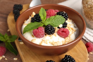 Photo of Tasty yogurt with granola and berries in bowl on wooden table, closeup
