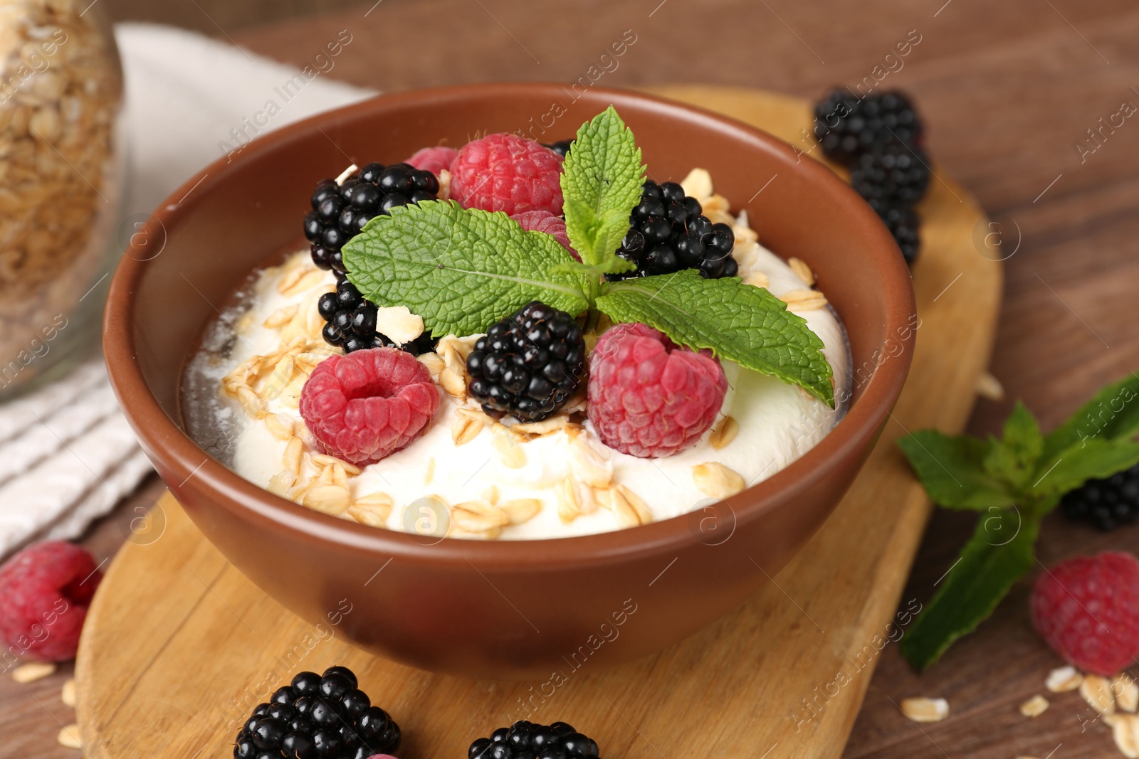Photo of Tasty yogurt with granola and berries in bowl on wooden table, closeup