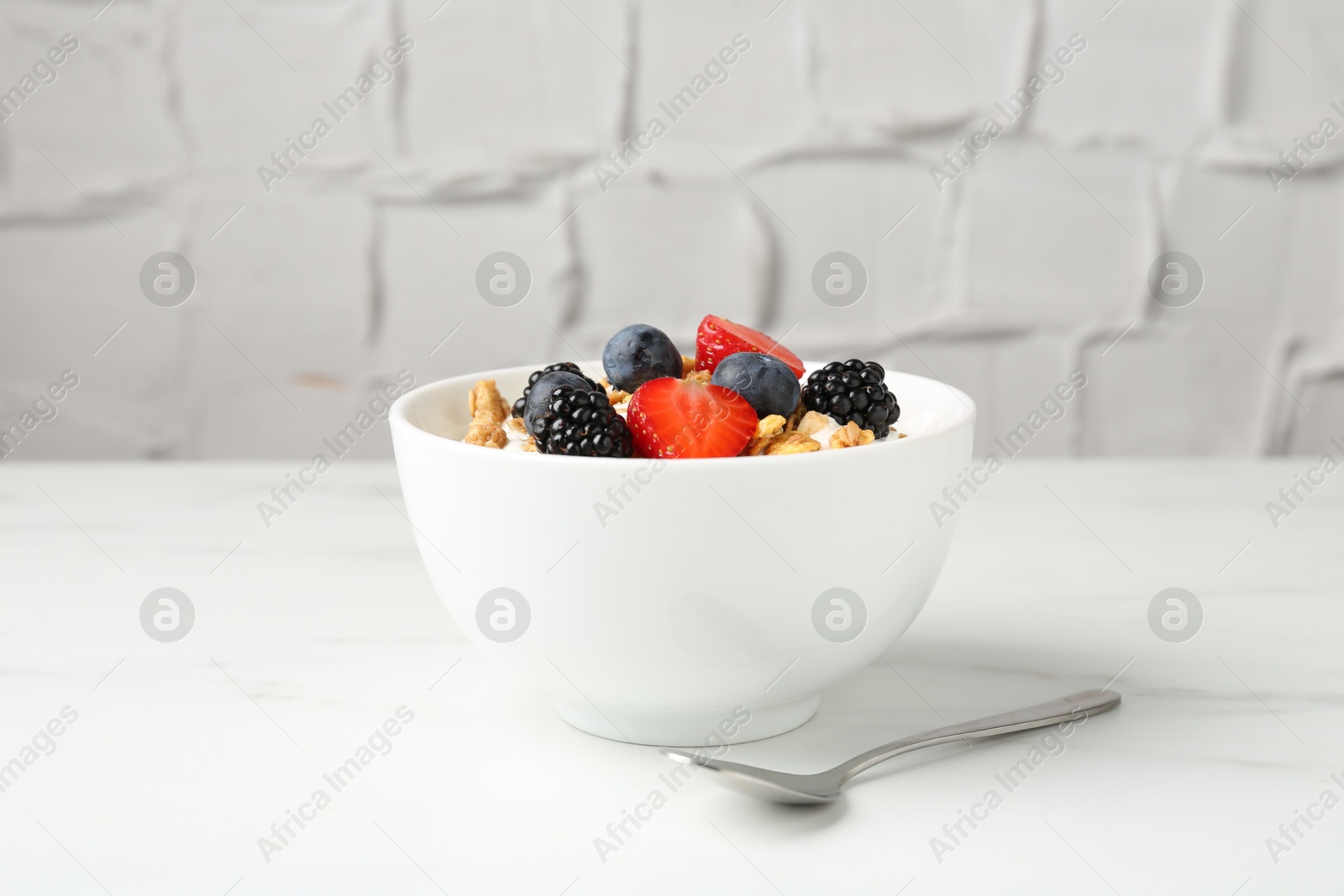 Tasty yogurt with granola and berries in bowl on white marble table, closeup Photo of Tasty yogurt with granola and berries in bowl on white marble table, closeup