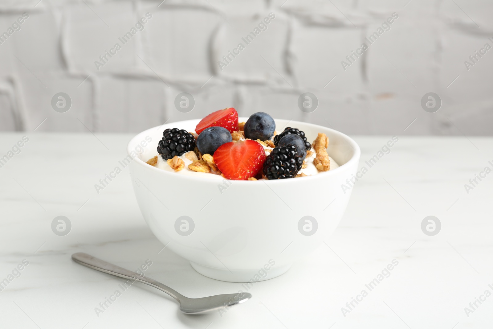 Photo of Tasty yogurt with granola and berries in bowl on white marble table, closeup